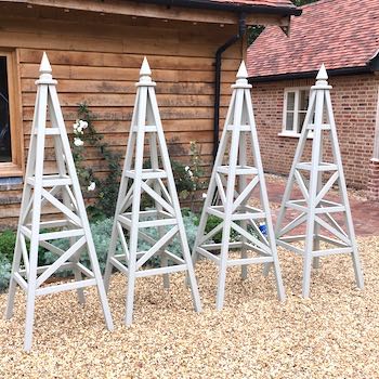 4 Chelsea Star Obelisks painted colour Hardwick White by Farrow & Ball, standing on gravel in front of flower bed and house