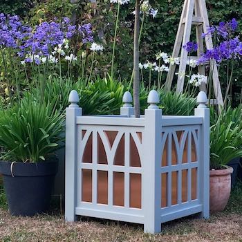 Gothic Style Planter with Copper Panels planted with Bay Tree and surrounded by blue and white Agapanthus flowers and wooden garden obelisks