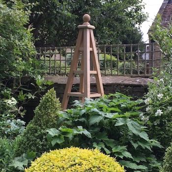 Large oak obelisk 8 foot tall with ball finial in garden with plants