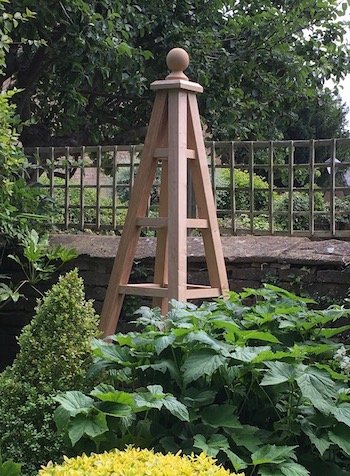 Large oak obelisk with ball finial in garden with plants