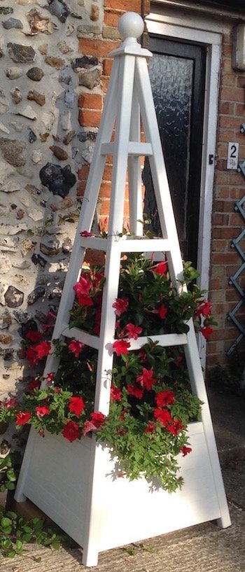 Obelisk with integral planter painted white with red flowers from the Mandeville plant